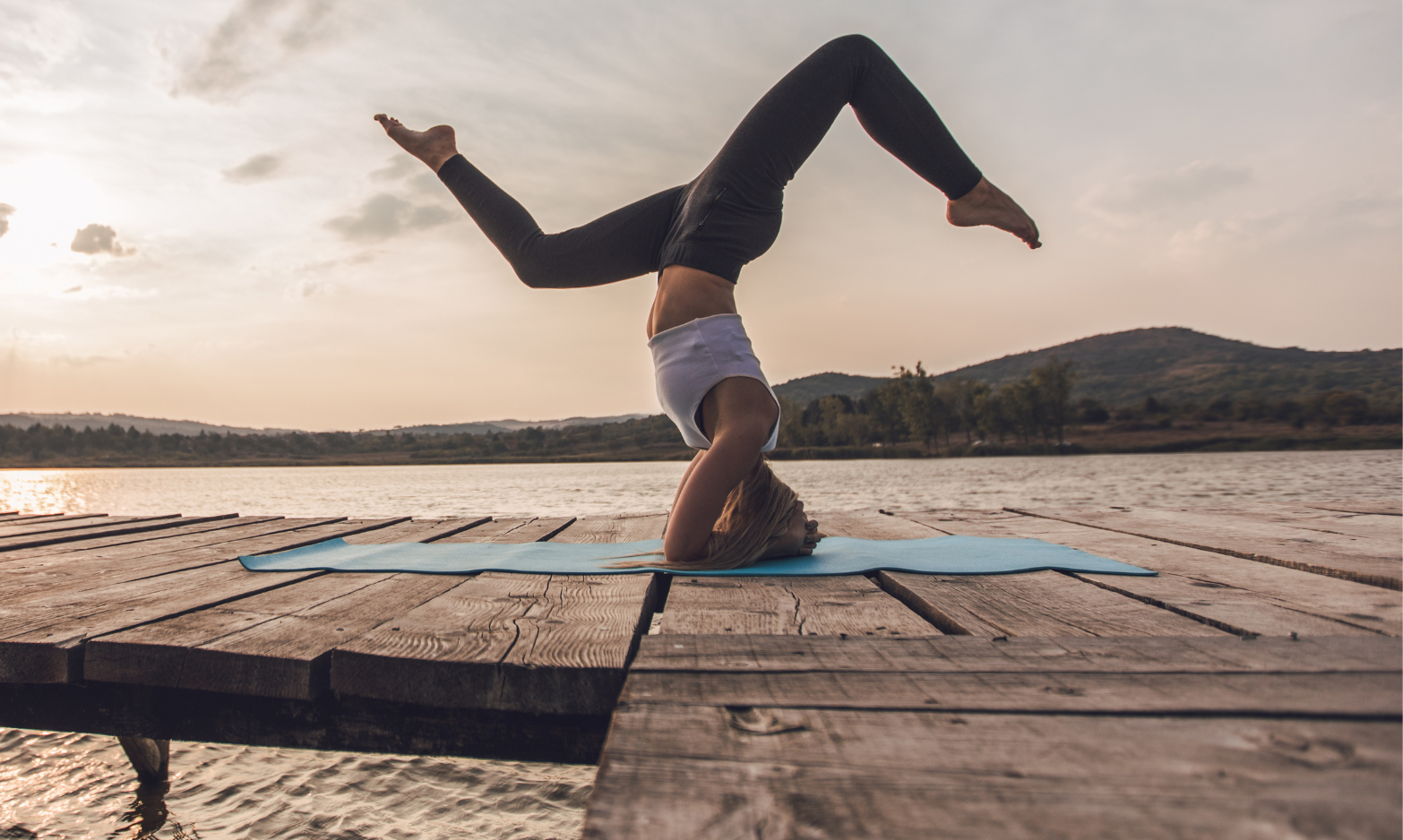 Woman in headstand yoga pose on a wooden pier at sunset