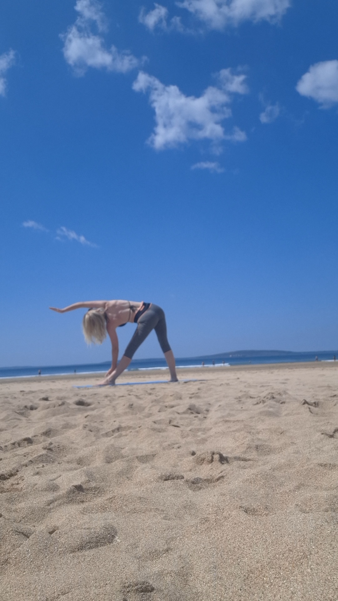 Jacqui in a triangle yoga pose on the beach under blue sky