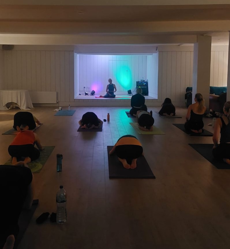 Class in child's pose facing Jacqui under aurora projections