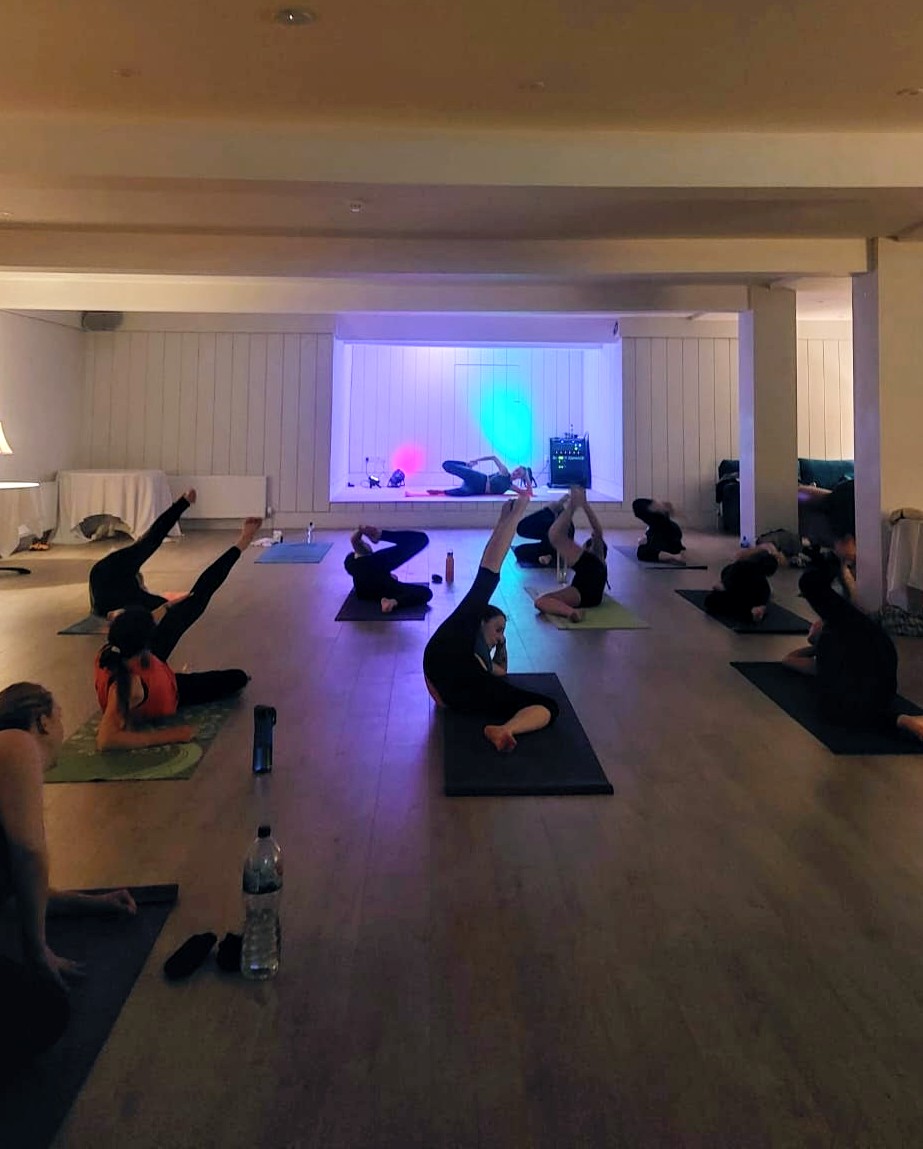 Yogis in a seated stretch lit by pink and teal stage lights